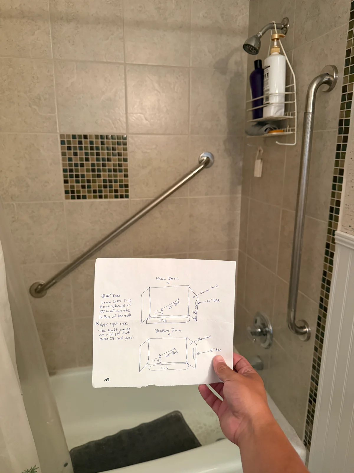 Grab bars installed in a tiled shower, with a handwritten installation plan held in the foreground