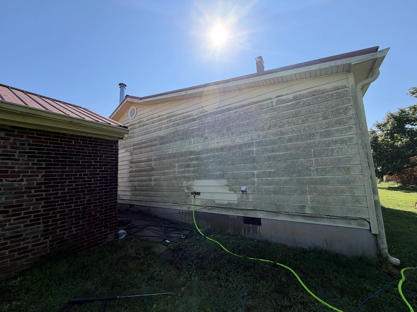 Heavy dark surface buildup on the yellow gable wall before house washing