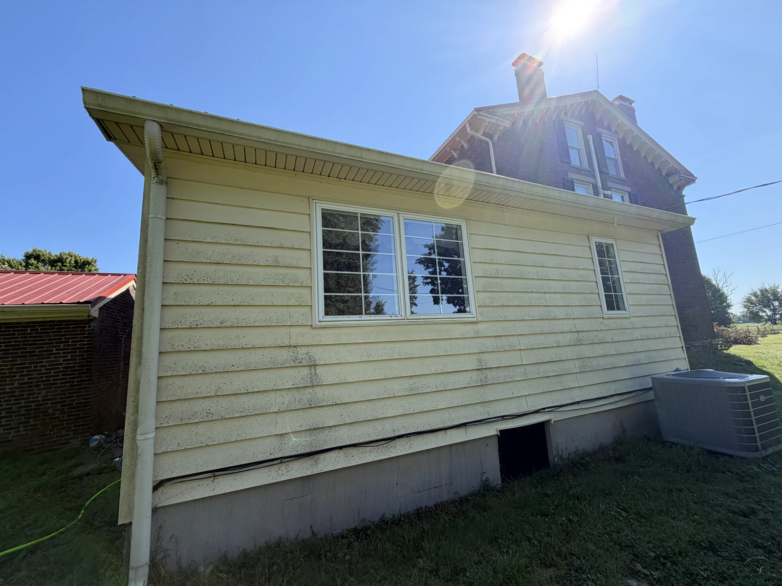 Yellow siding with dark surface buildup around two windows before house washing