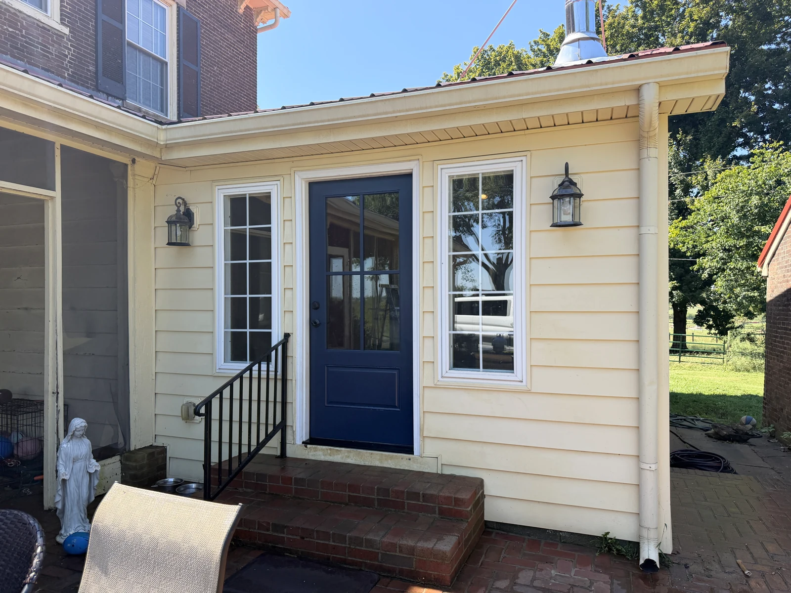 Yellow siding and white window trim around a blue entry door after washing
