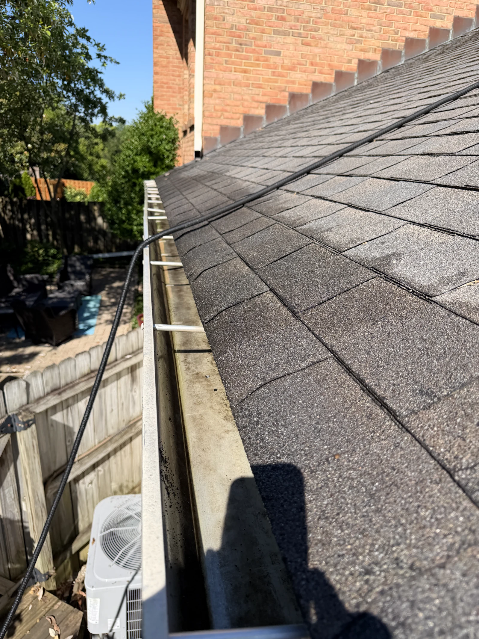 Open rear roof gutter after debris removal with a hose alongside the shingles