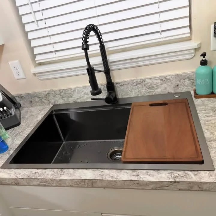 Installed black workstation sink with a spring-style faucet and wood cutting board